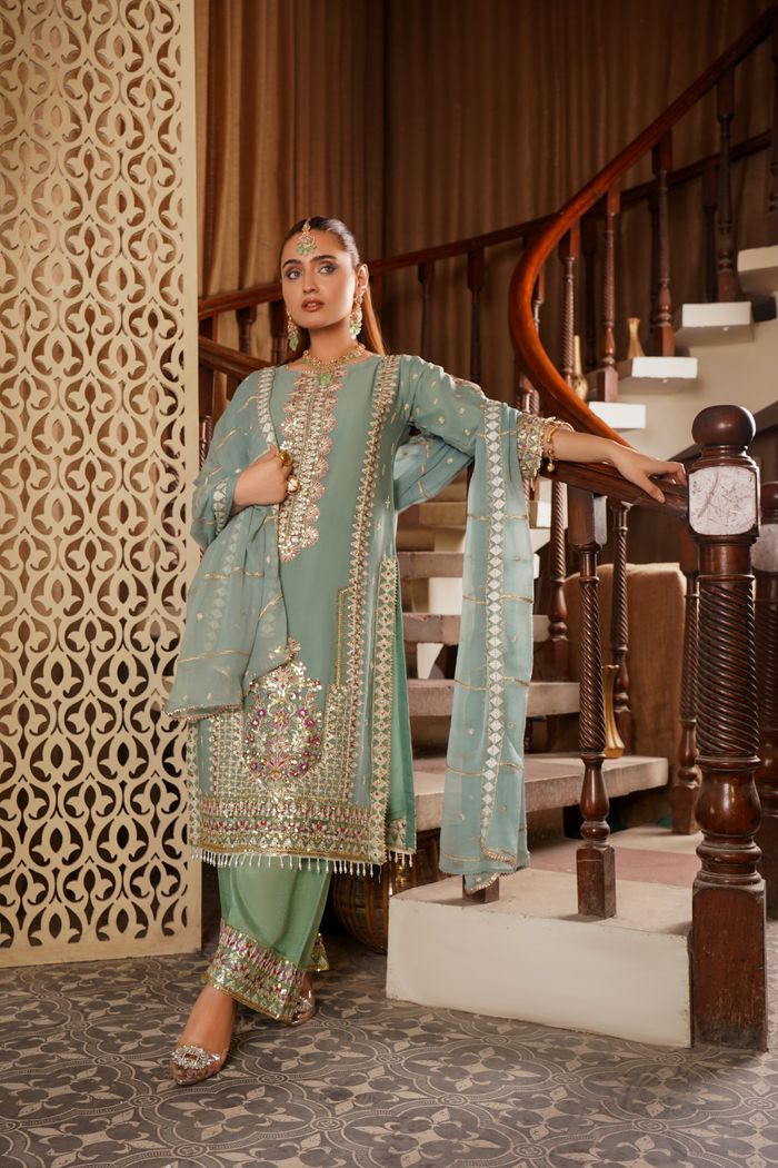 A graceful woman in traditional South Asian bridal attire poses indoors on a staircase.